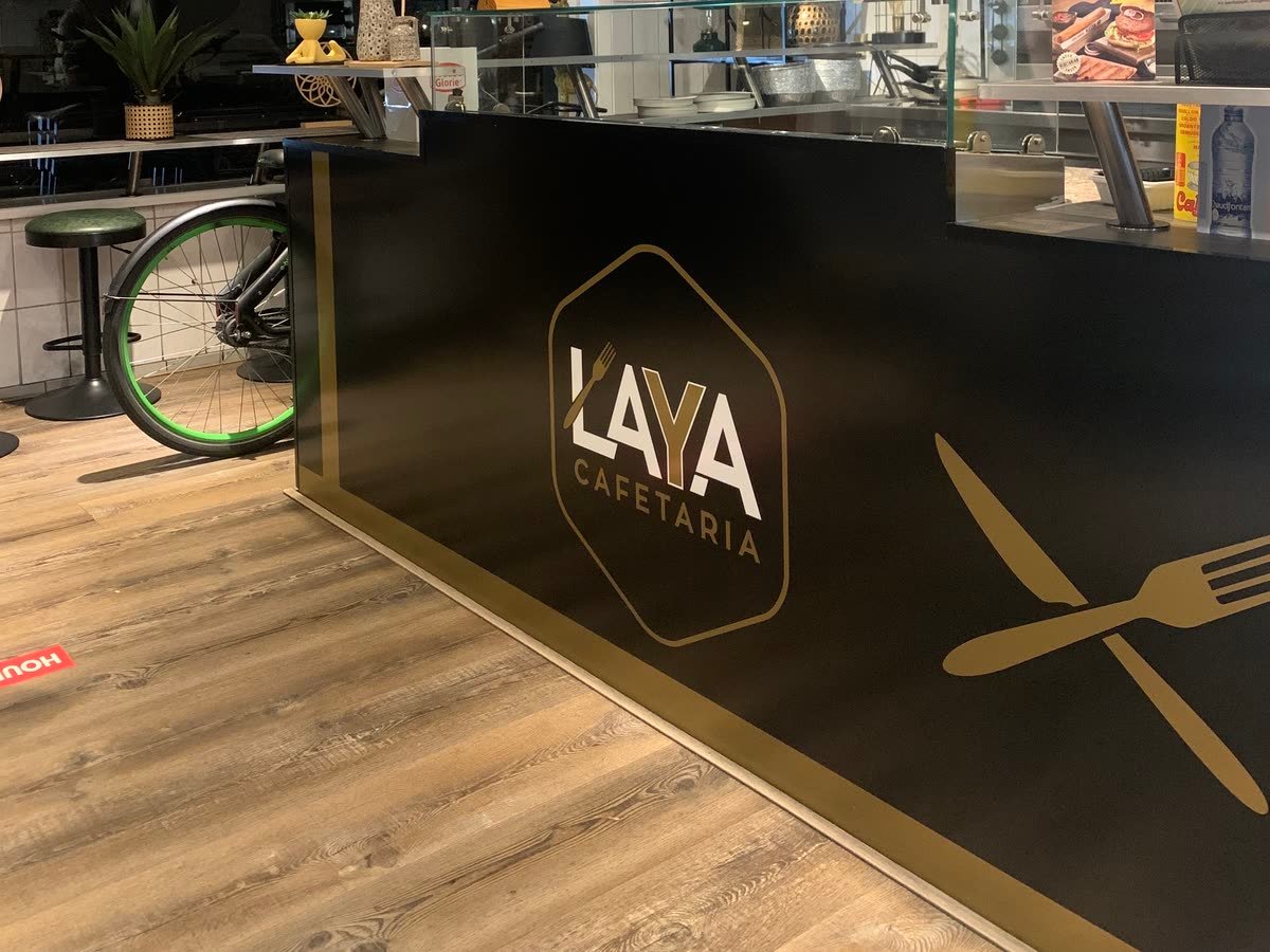 De zwarte toonbank van Cafetaria Laya met het zeshoeklogo en een gouden mes en vork.